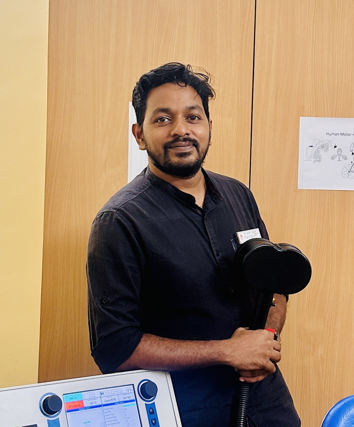 Jithin Joseph in a clinical setting, holding a brain stimulation device